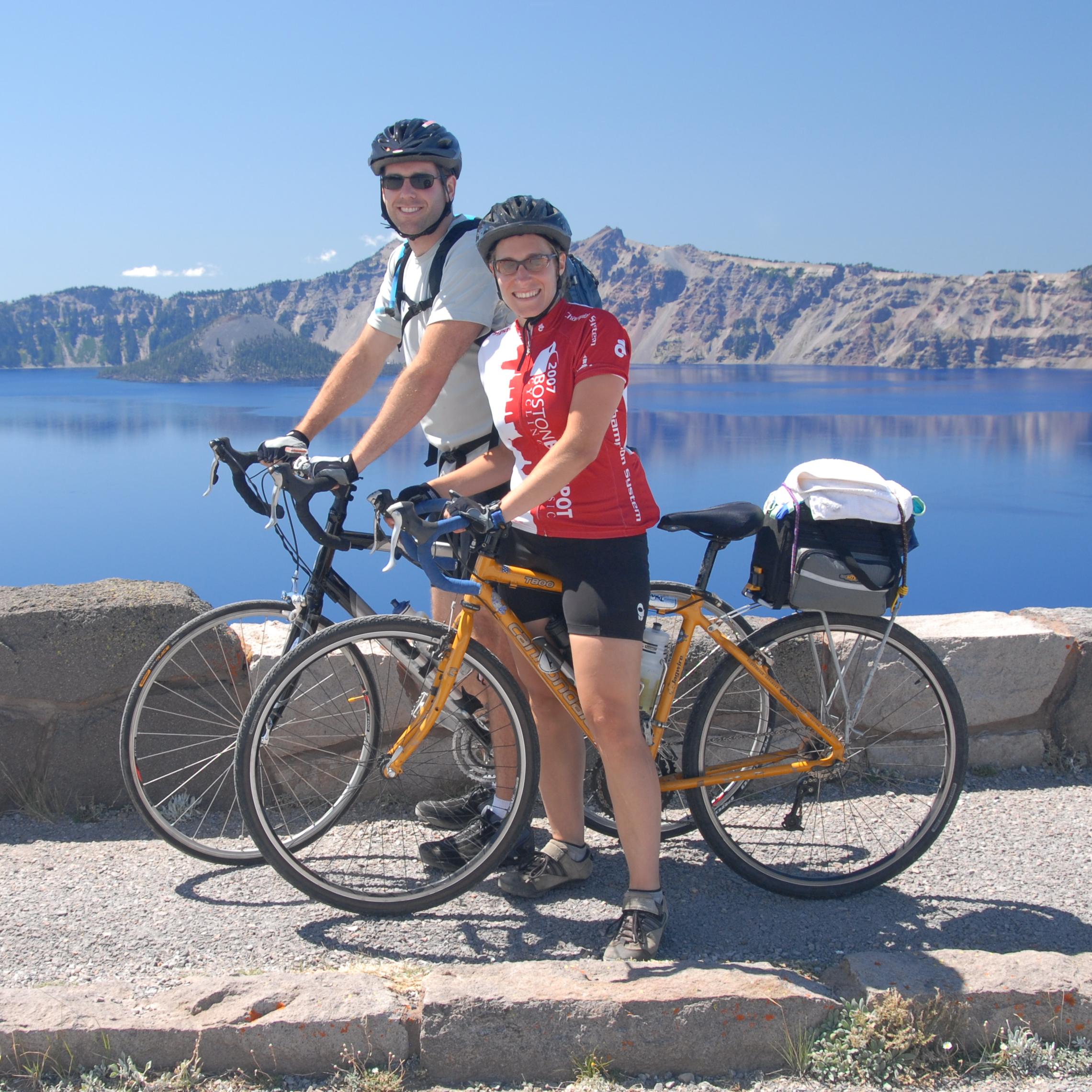 Two visitors on bikes with Crater Lake in the background.