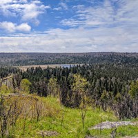 Cloudy skies overlook forested ridges and a creek in the distance.