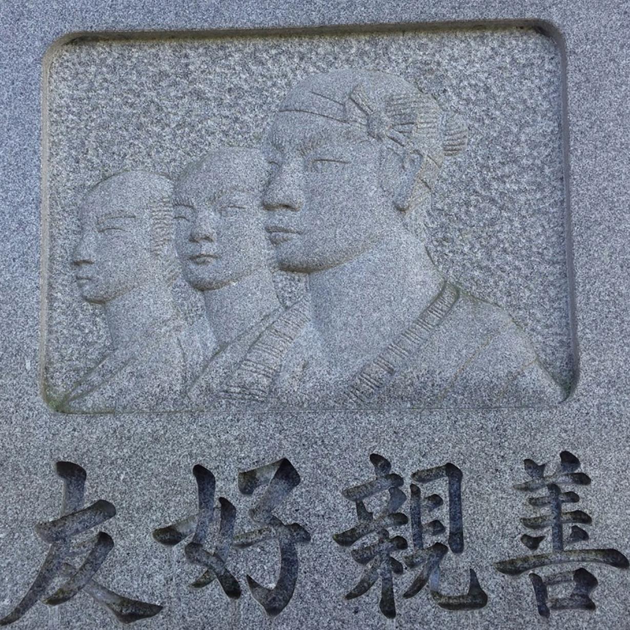 A photo of a stone monument with a carving of three Japanese sailors and text in Japanese.