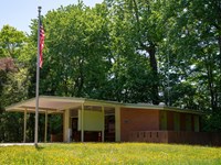 A single story sheltered enclosure with interpretive panels and a flag outside.