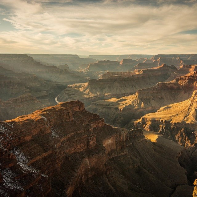 View of the Grand Canyon from the top of the rim. Low angled light rays hit the edge of the canyon. 