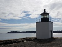 White lighthouse 12 feet square and 20 feet tall with red flashing light with water on 3 sides