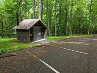 Brown building by parking area with two doors. The doors are labeled with restroom signs.