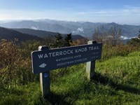 Wooden sign reading Waterrock Knob Trail with rolling mountains in distance