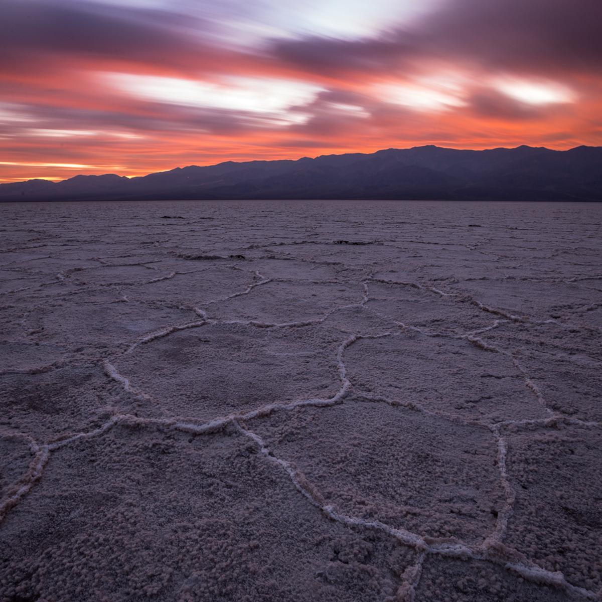 An expansive salt flat with distant desert mountains and a pink sky sunset. 