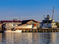 Boats docked at the Chesapeake Bay Maritime Museum with buildings and lighthouse in the background.