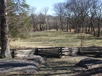 A cedar rail fence cuts across a grass covered slope. A river runs at the base of the slope.
