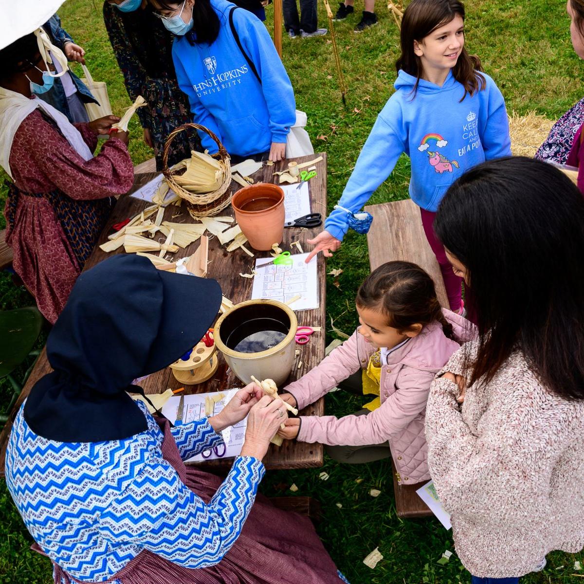 Living historians help a child make a corn husk doll