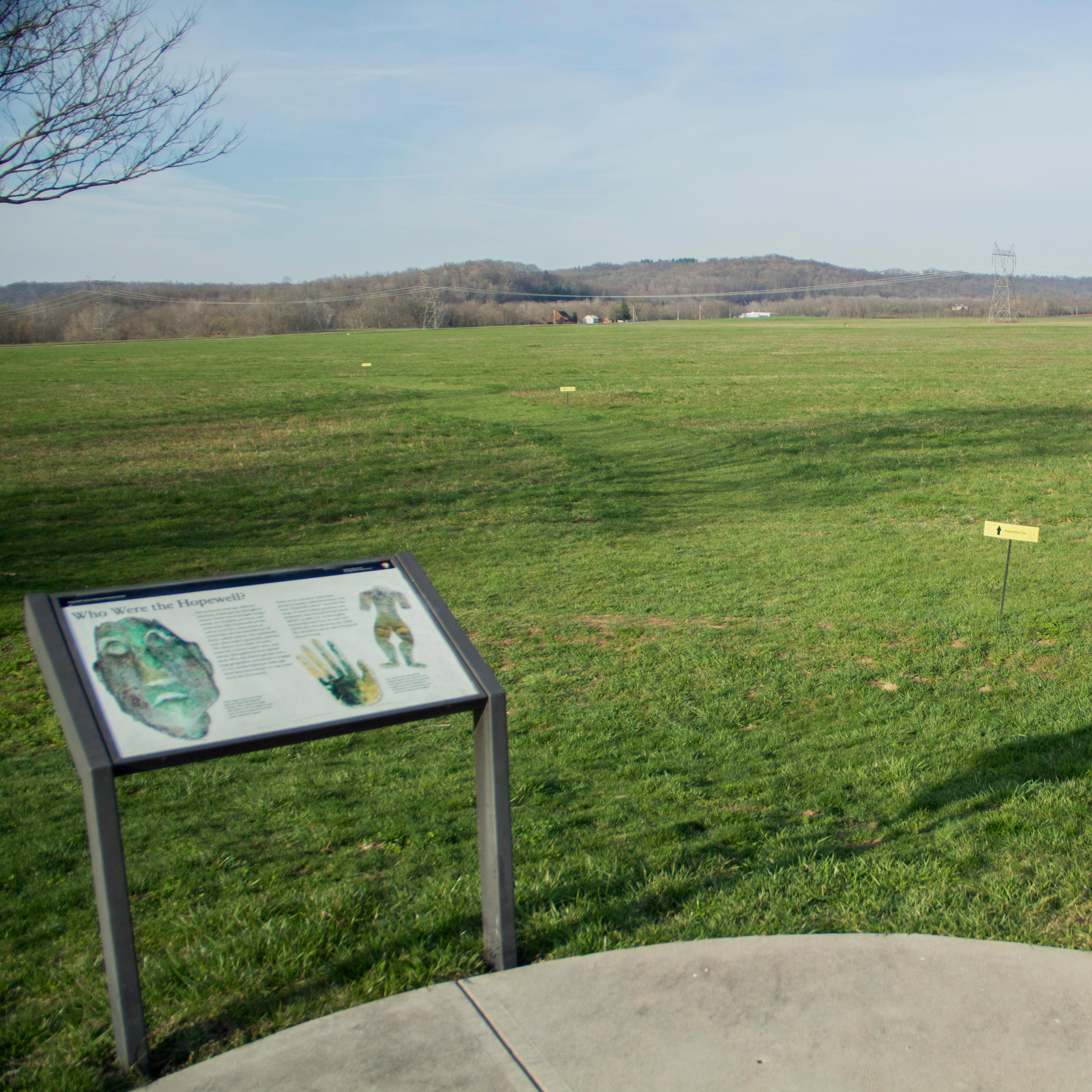 Two interpretive signs in the foreground with a large green field in the background