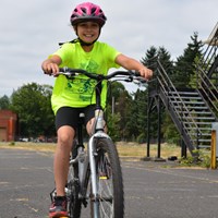 A child on a bicycle wearing a pink helmet.