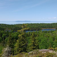 View from a ridge overlooking an interior lake, a forest, Lake Superior, and Canada\'s shoreline.