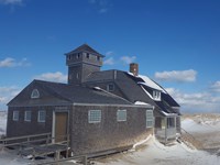 A historic building with a tower and cedar shakes stands against snow and a deep blue sky.