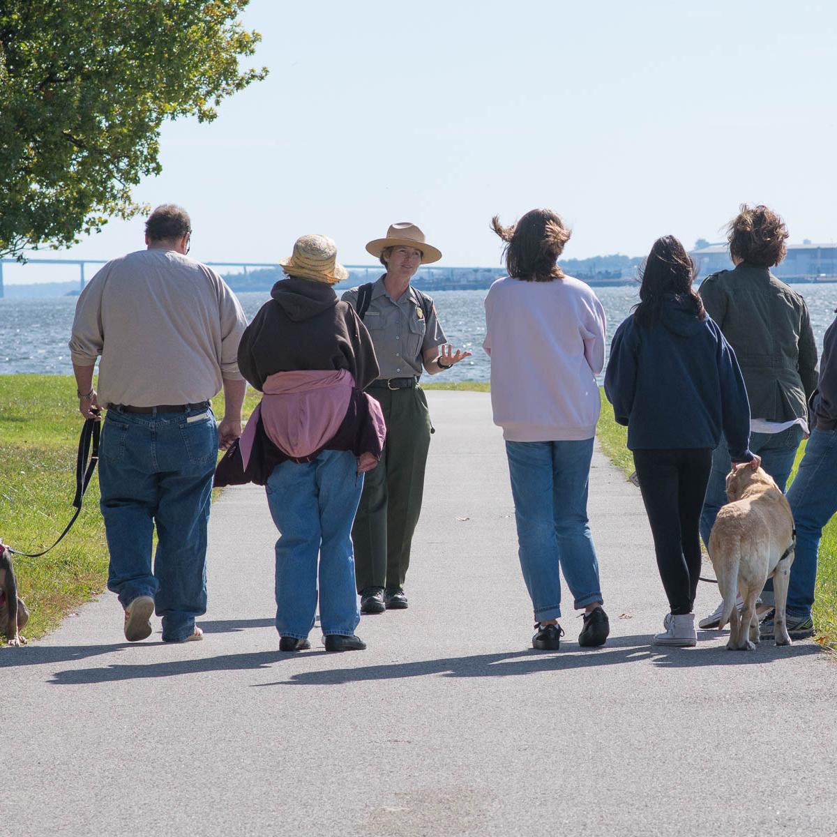 A ranger walking with visitors on the seawall trail. Several have dogs on leashes.