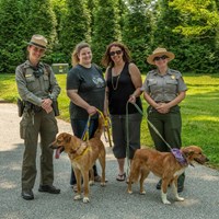 Two visitors with dogs on leashes pose with two park rangers.