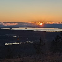 A view of a sunset from the top of a mountain, looking towards the ocean and islands.