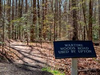 A sign with text, "Wartime Roads Used by Upton" and a trail going through the woods.