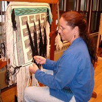 A woman demonstrates tradition weaving technique on a loom