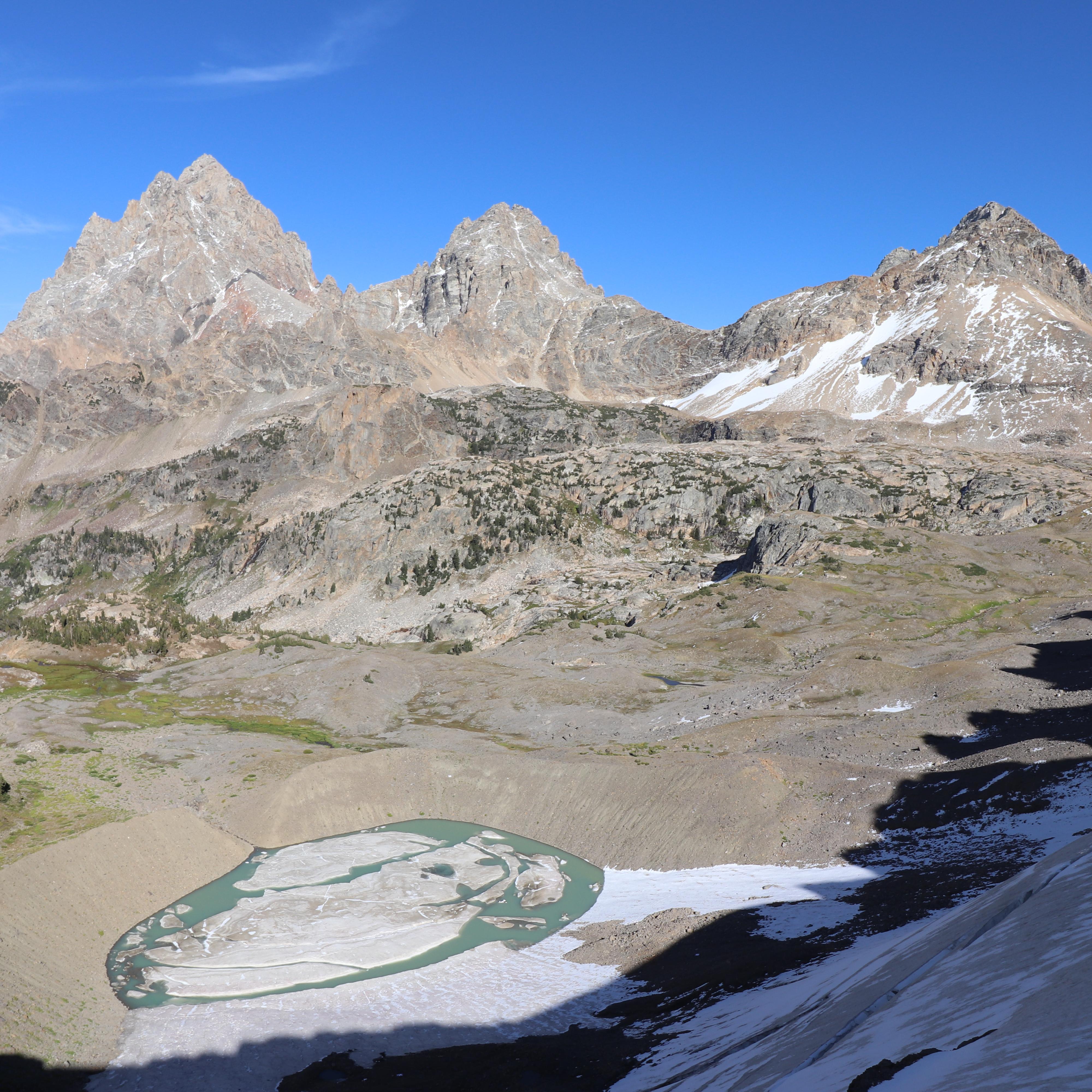 3 mountain peaks stand tall above a glacially carved valley, a glacial lake, and a small glacier. 