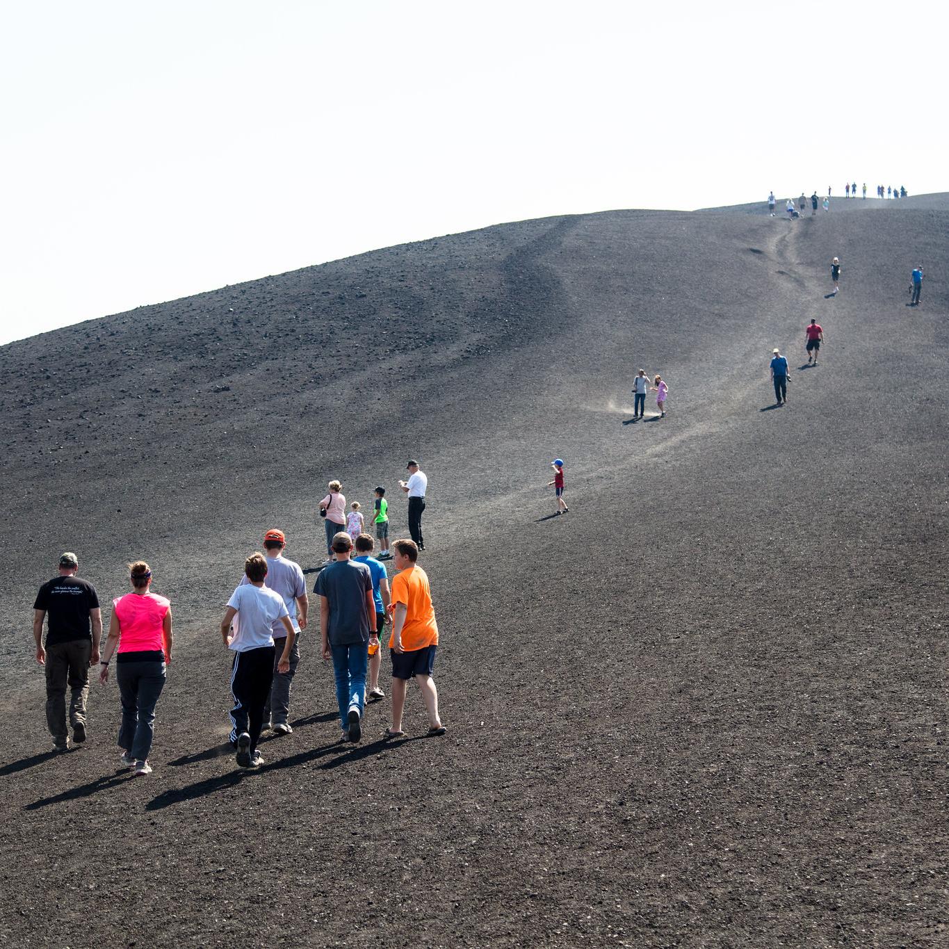 Visitors start a steep climb up a bare cinder slope.