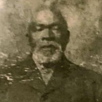 Faded B&W photo of black man with gray gotee and a black button overcoat.