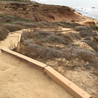 A long downward set of steps along a dirt path going towards the ocean.