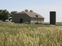 A three story stone barn stands beyond the grass field.