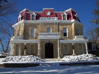 A three story stone house with steep red roof powdered in snow.