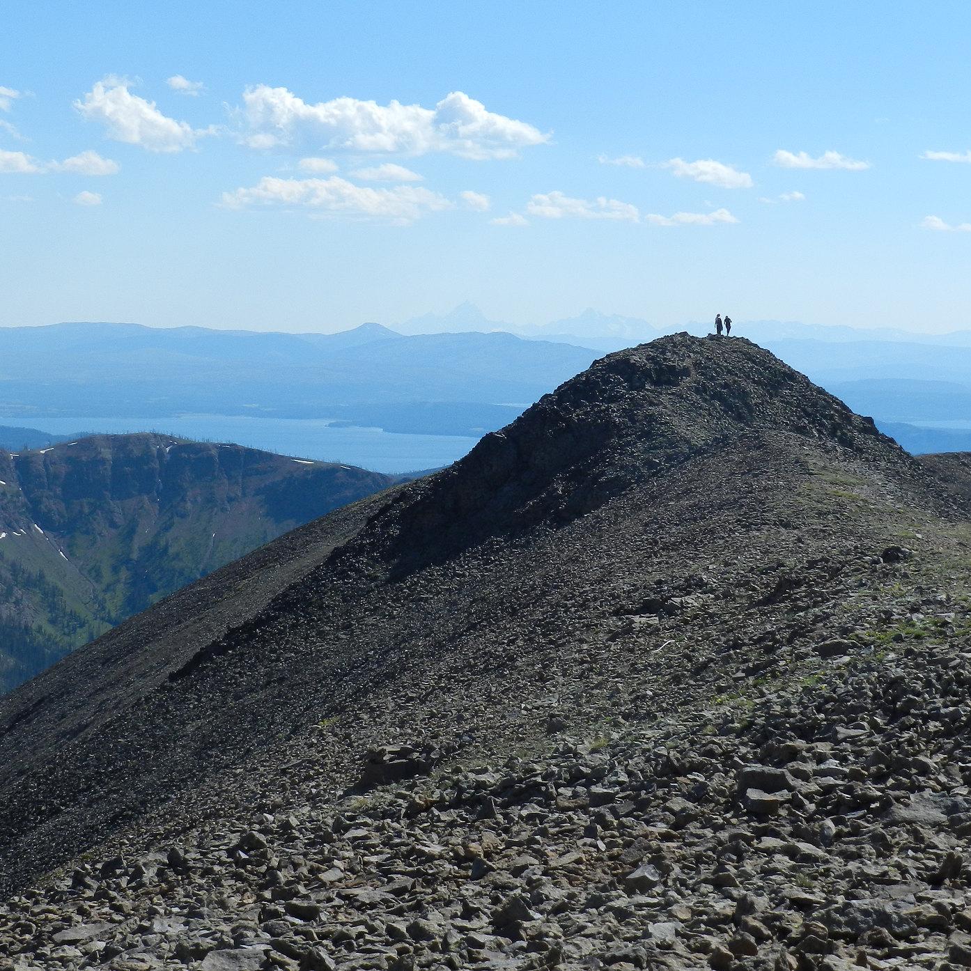 Two hikers enjoying the view of mountains in the distance from the summit of rocky mountain.
