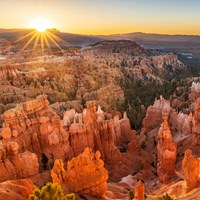 Looking down from above over a scenery of irregular red rocks with the sun rising behind them