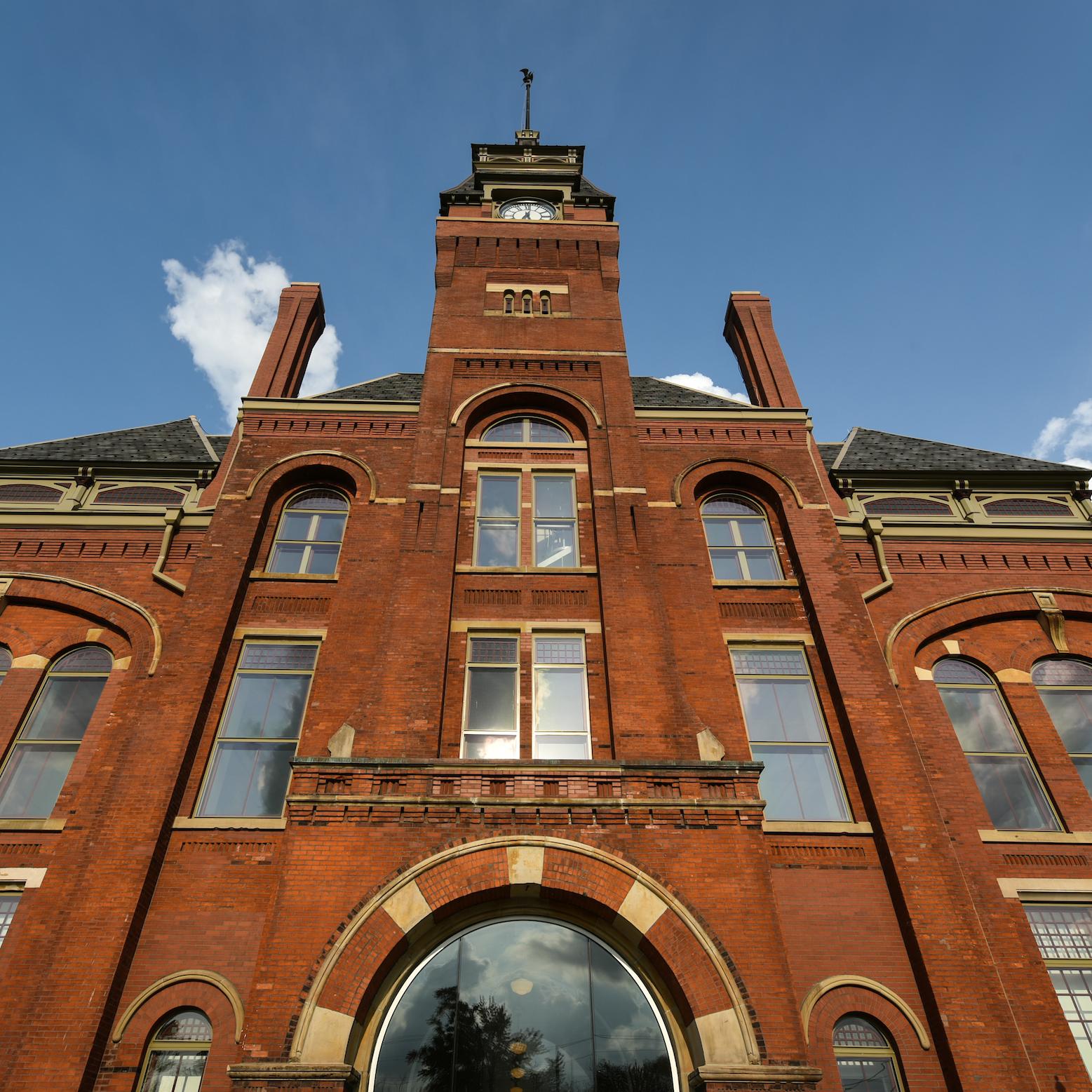 A red brick four story building with a clock tower stands tall against a partly cloudy sky.