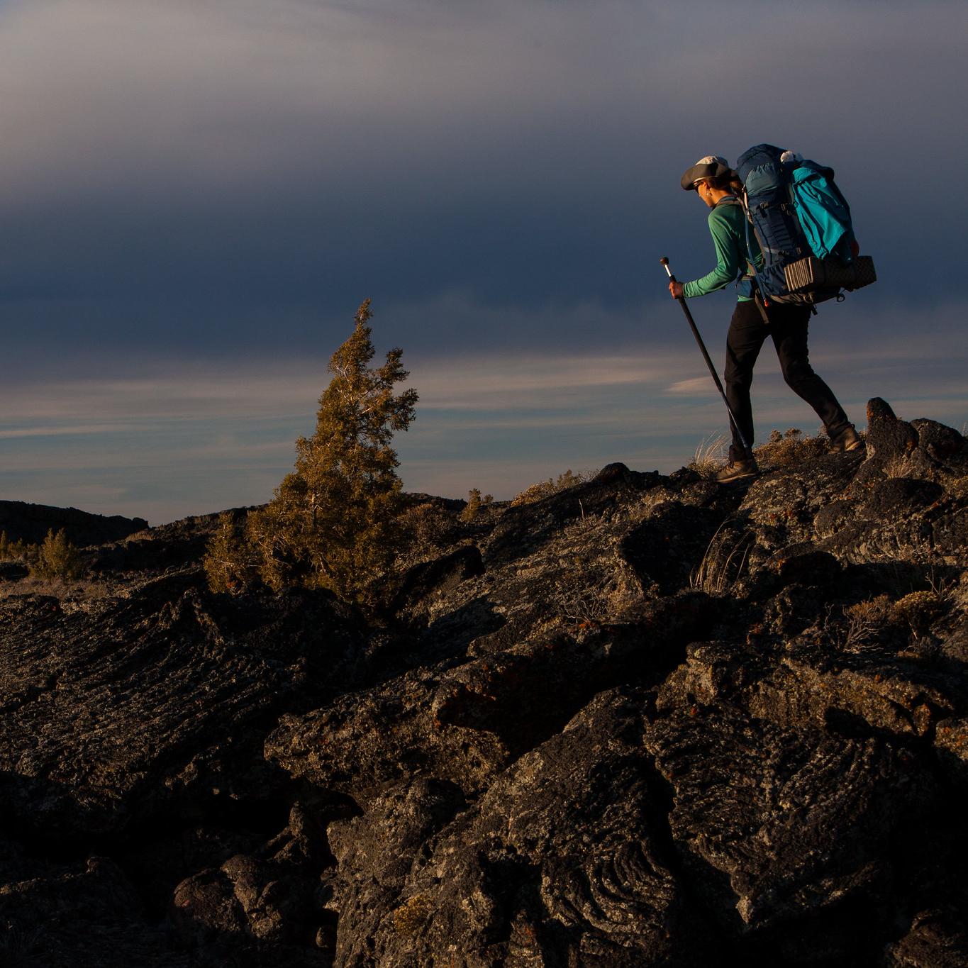 A hiker with a large backpack traverses a lava field.
