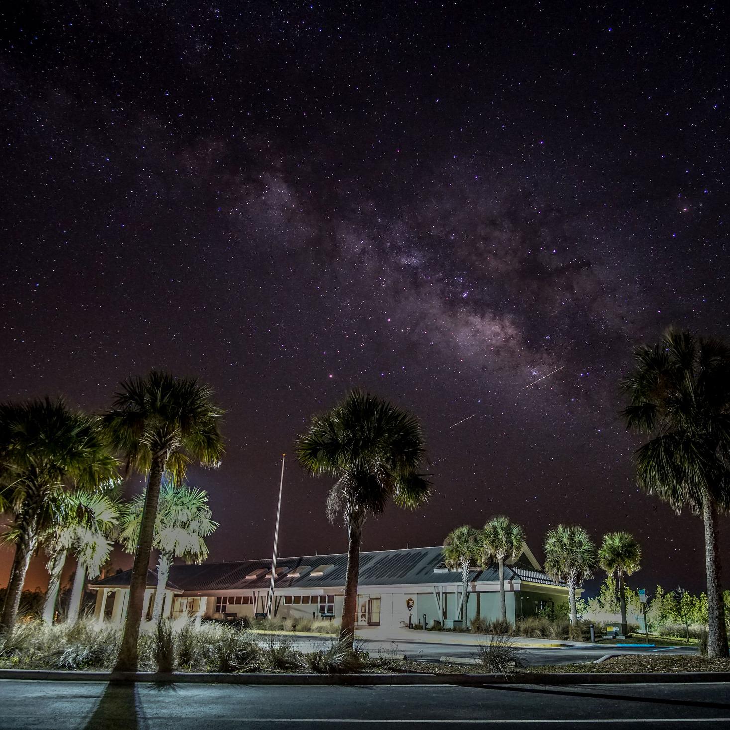 Visitor Center illuminated at night with night sky visible and palm trees in the foreground