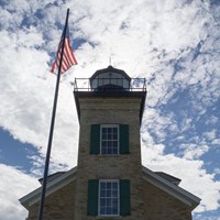 A lighthouse front is in shadows in front of a bright, cloudy sky