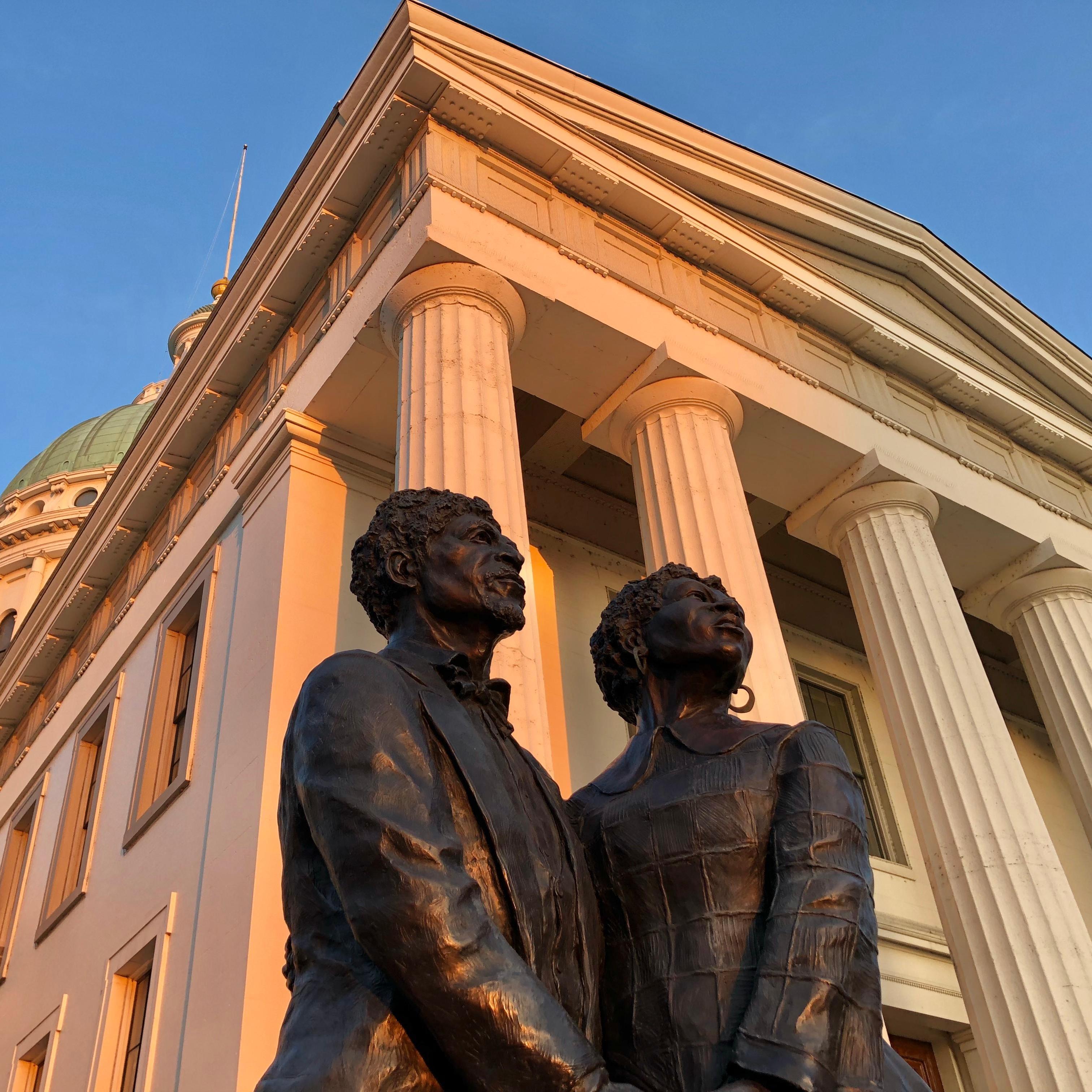 Gateway Arch from below illuminated by orange light against a blue, cloudy sky. 