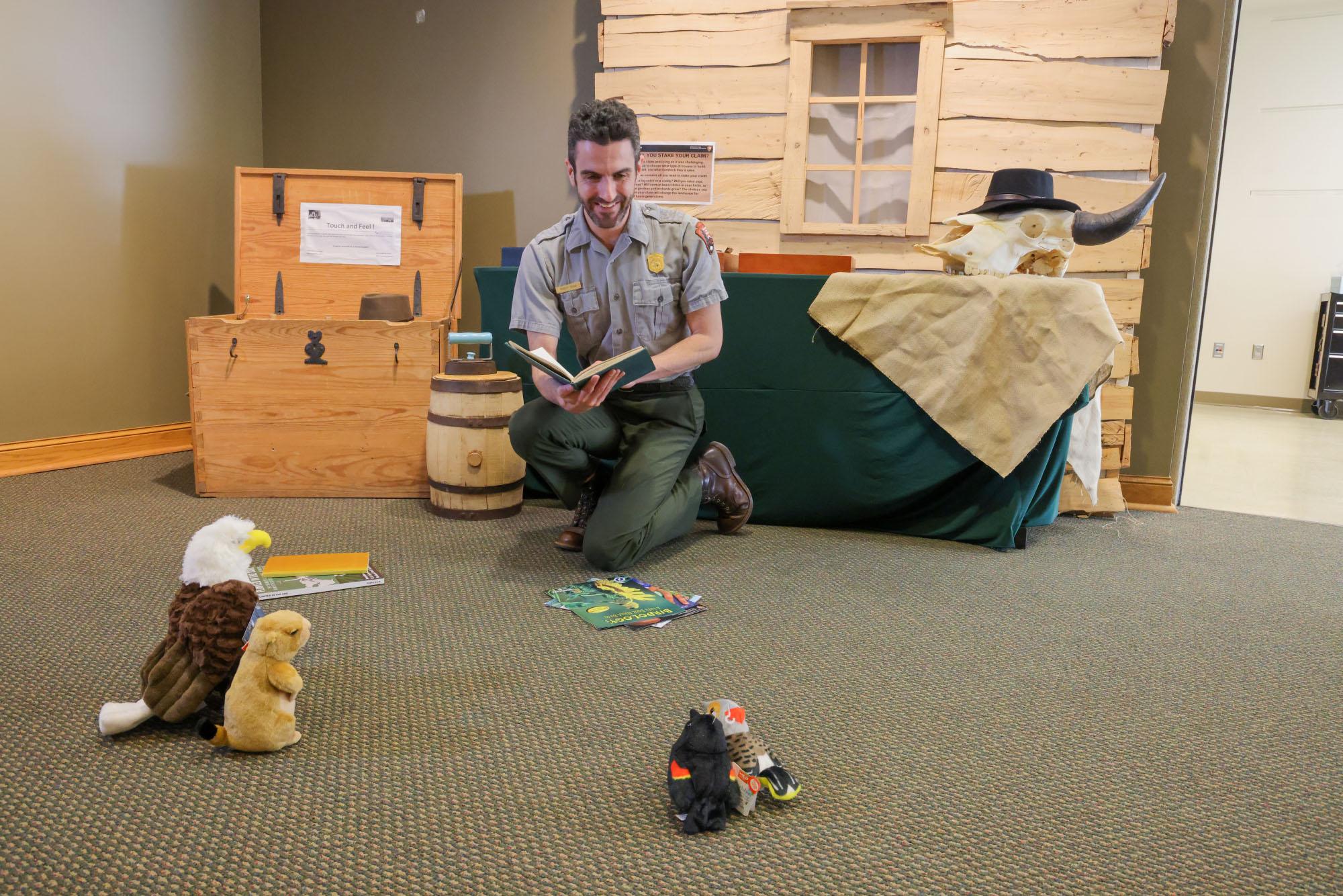 Uniformed NPS ranger reads to stuffed animals in an indoor setting.