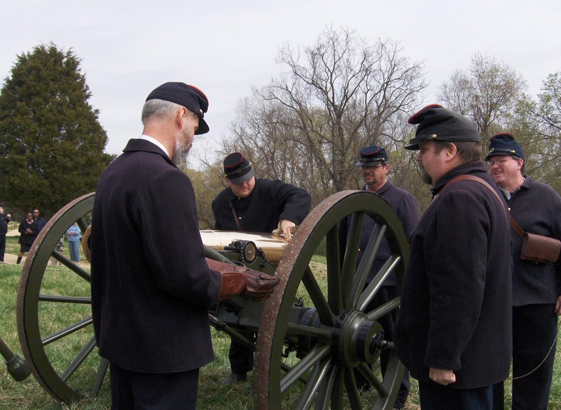 Volunteers in Civil War Union Army uniforms drilling on the cannon.