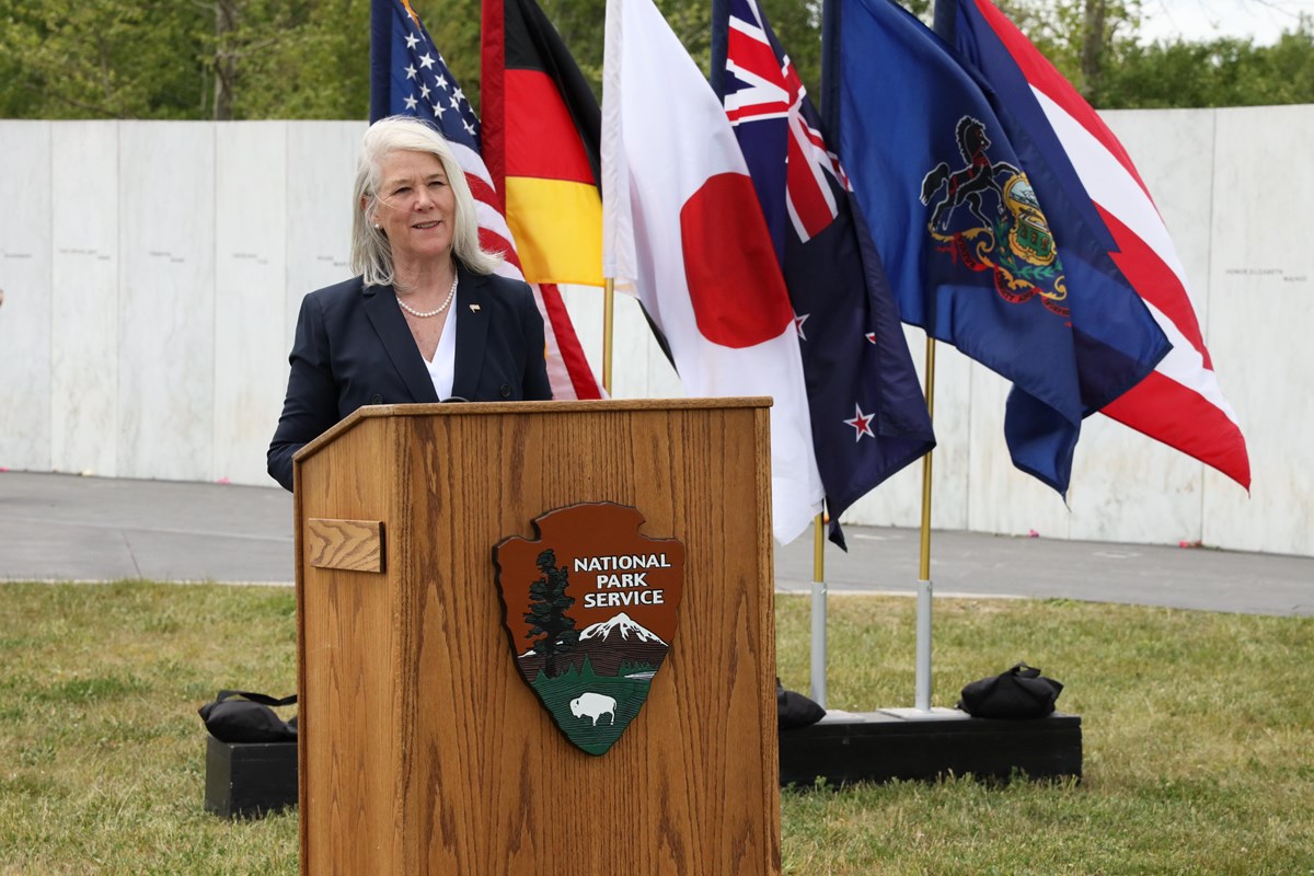 Woman standing at podium in front of flags.