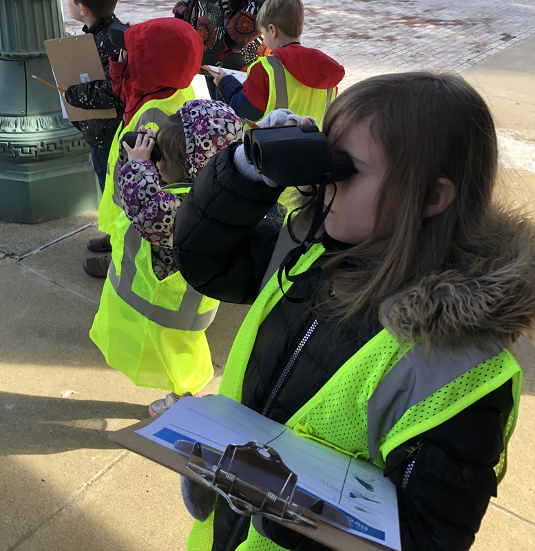 Children in high visibility vests look through binoculars.