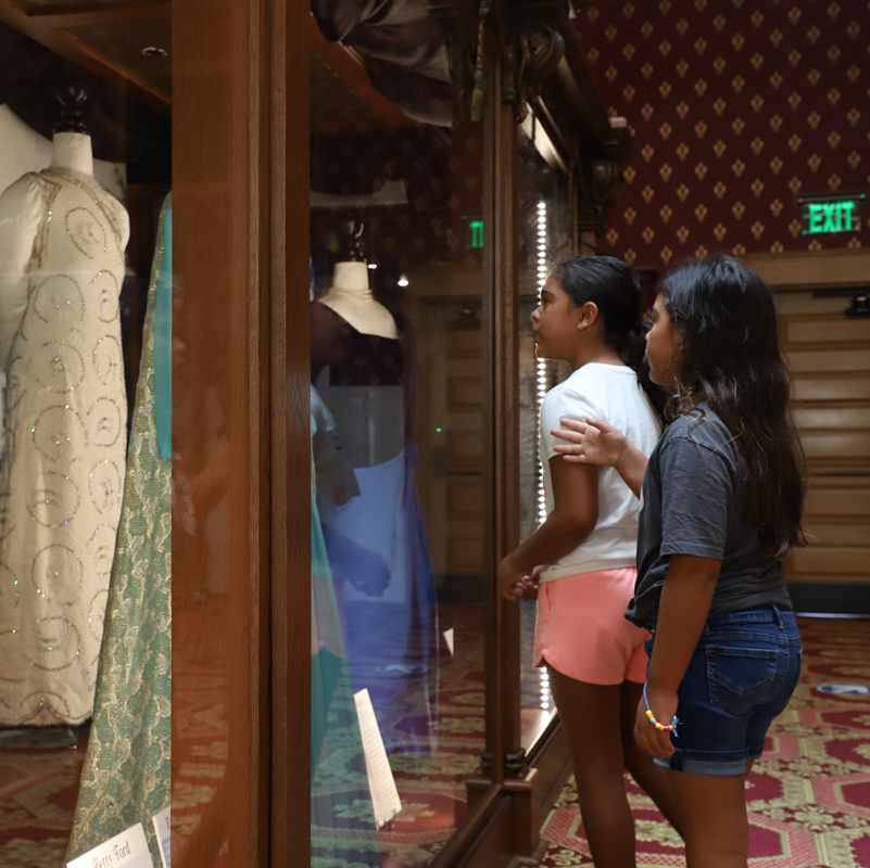Two girls look at a case containing first lady clothing.