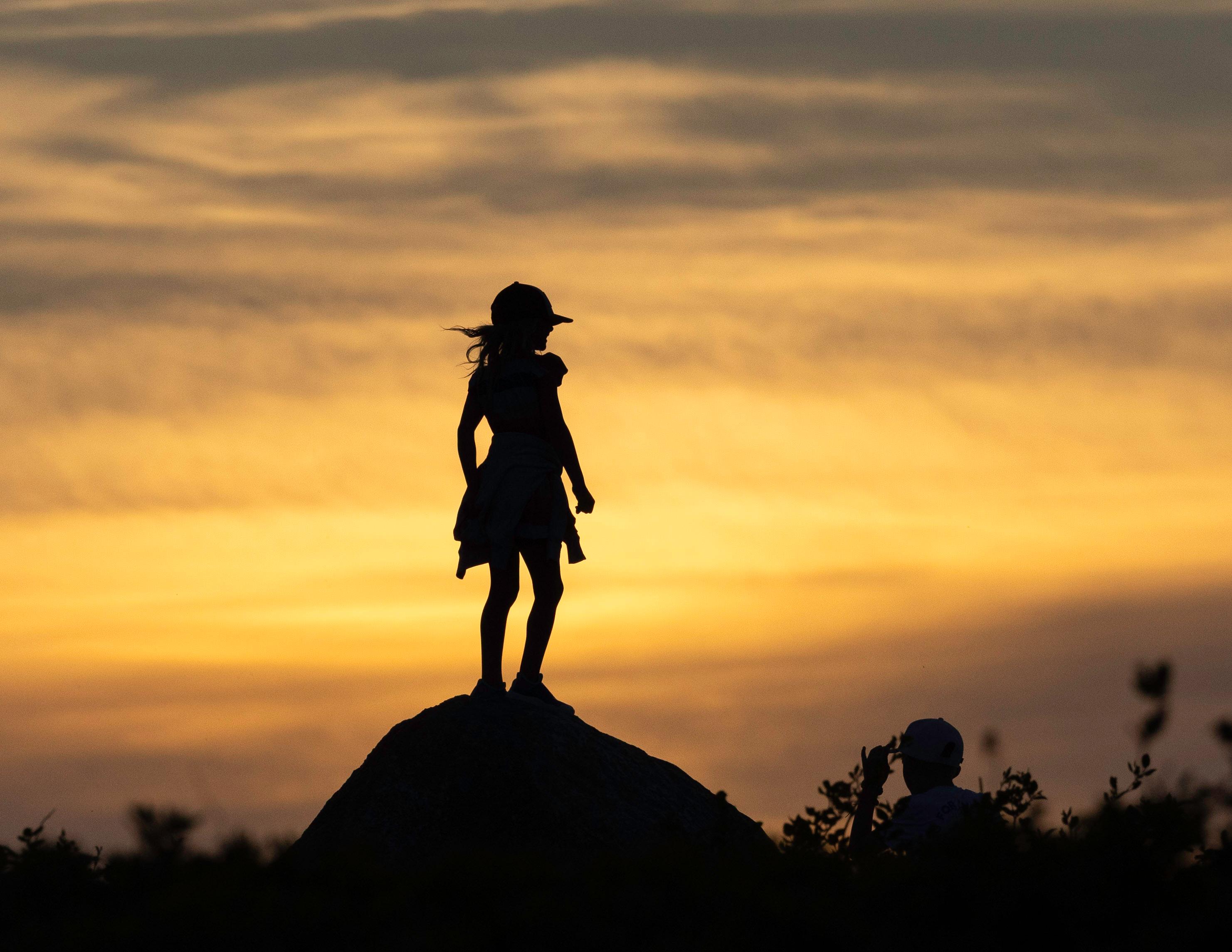 Dynamic photo of a girl's silhouette standing on a rock with the sunset in the background.
