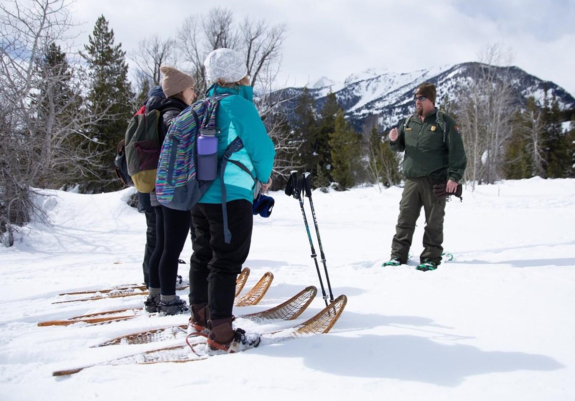 Visitors in wood snowshoes with a ranger on deep fresh powder snow with mountains behind.