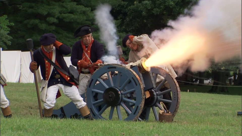 From a Distance, a half dozen men surround a cannon that explodes with fire in front of them
