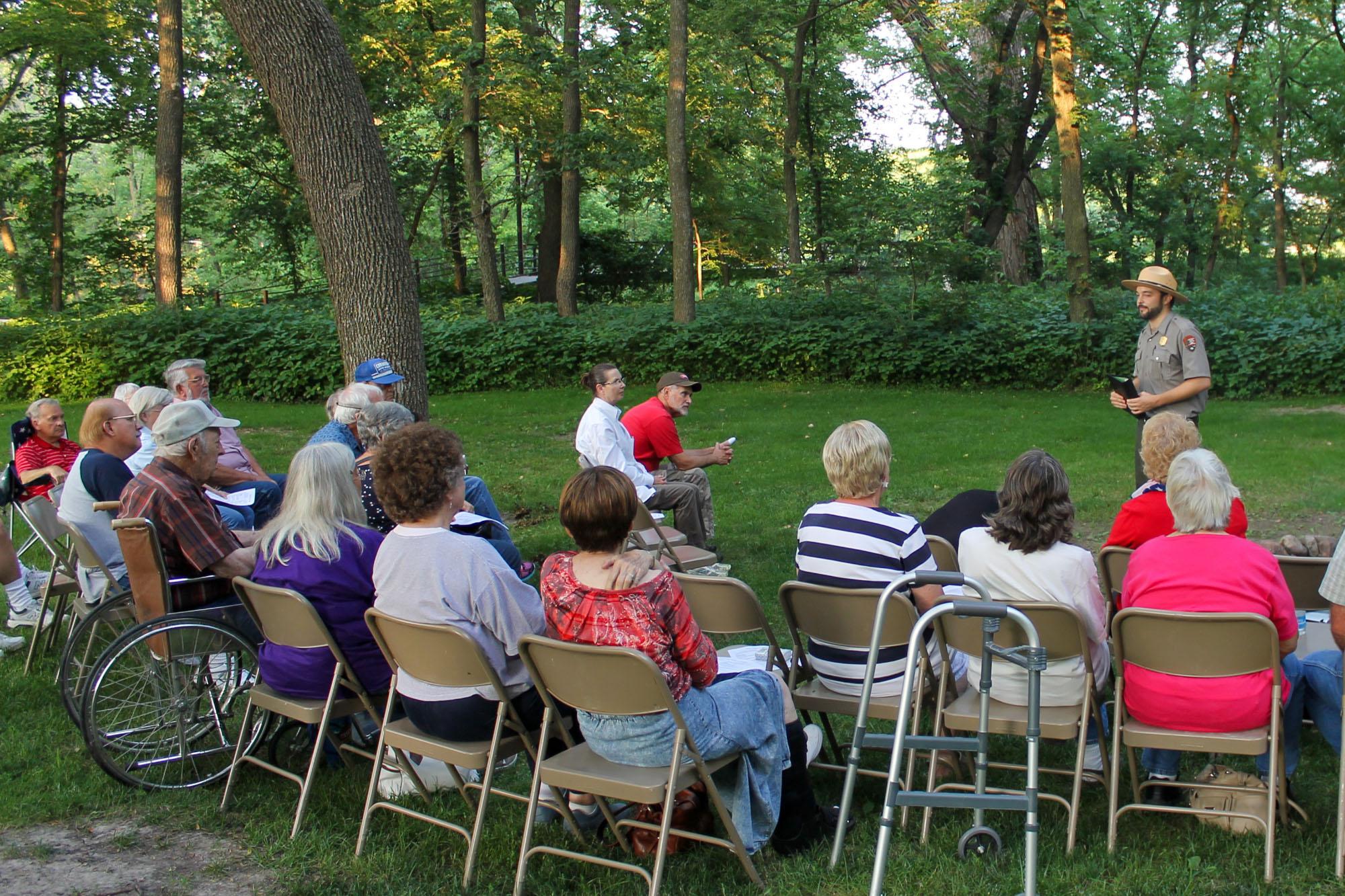 Uniformed park ranger speaks to a gathered audience in an outdoor setting.