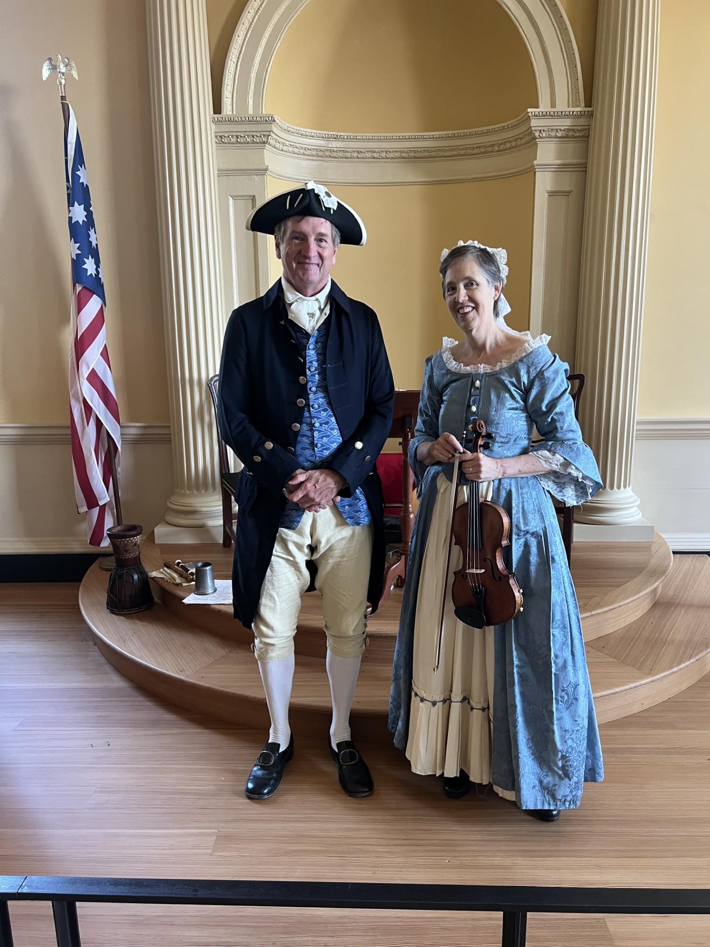 A man stands next to a woman holding a violin. They both smile.