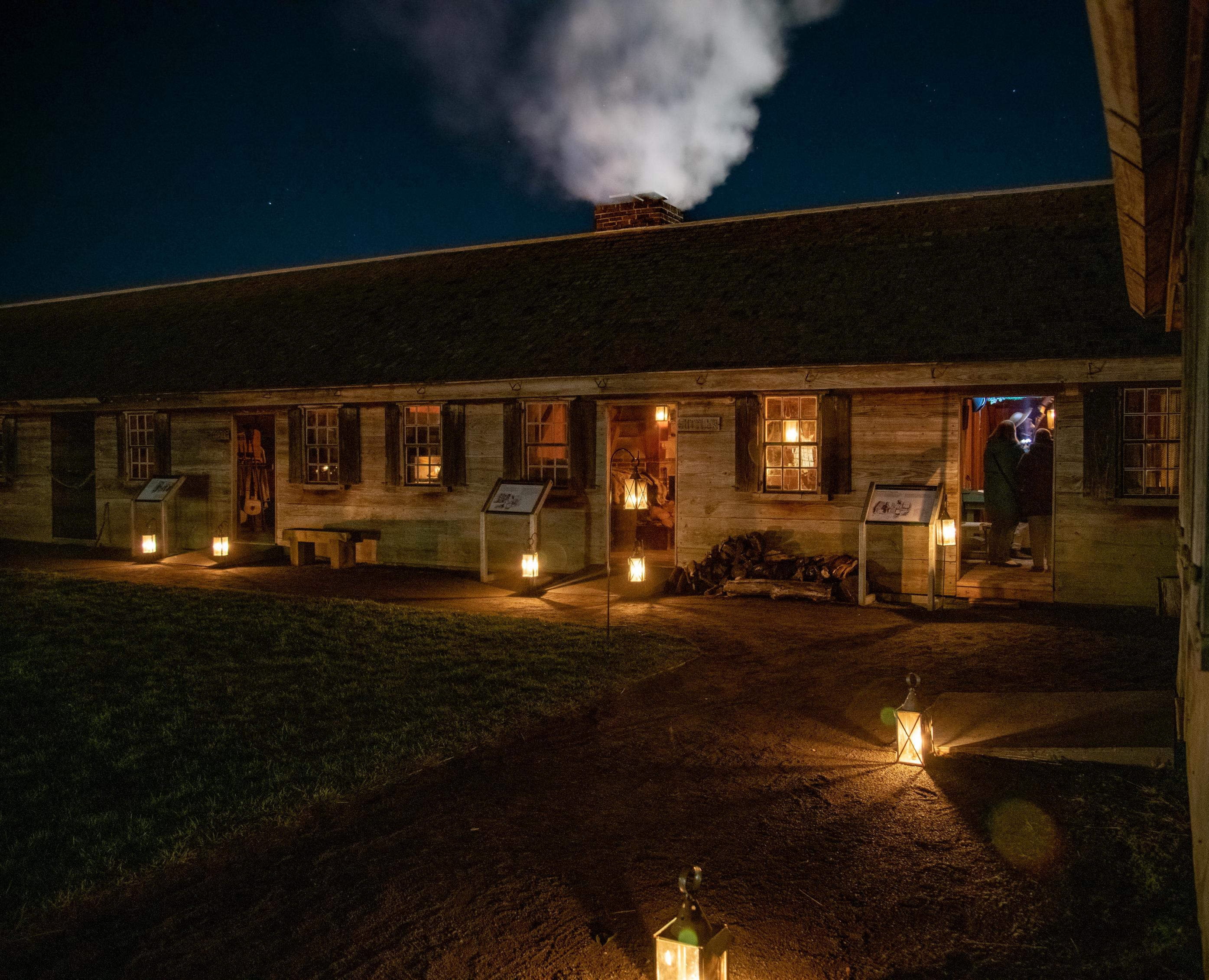 Candles in lanterns pour a golden light onto a darkened wooden building.
