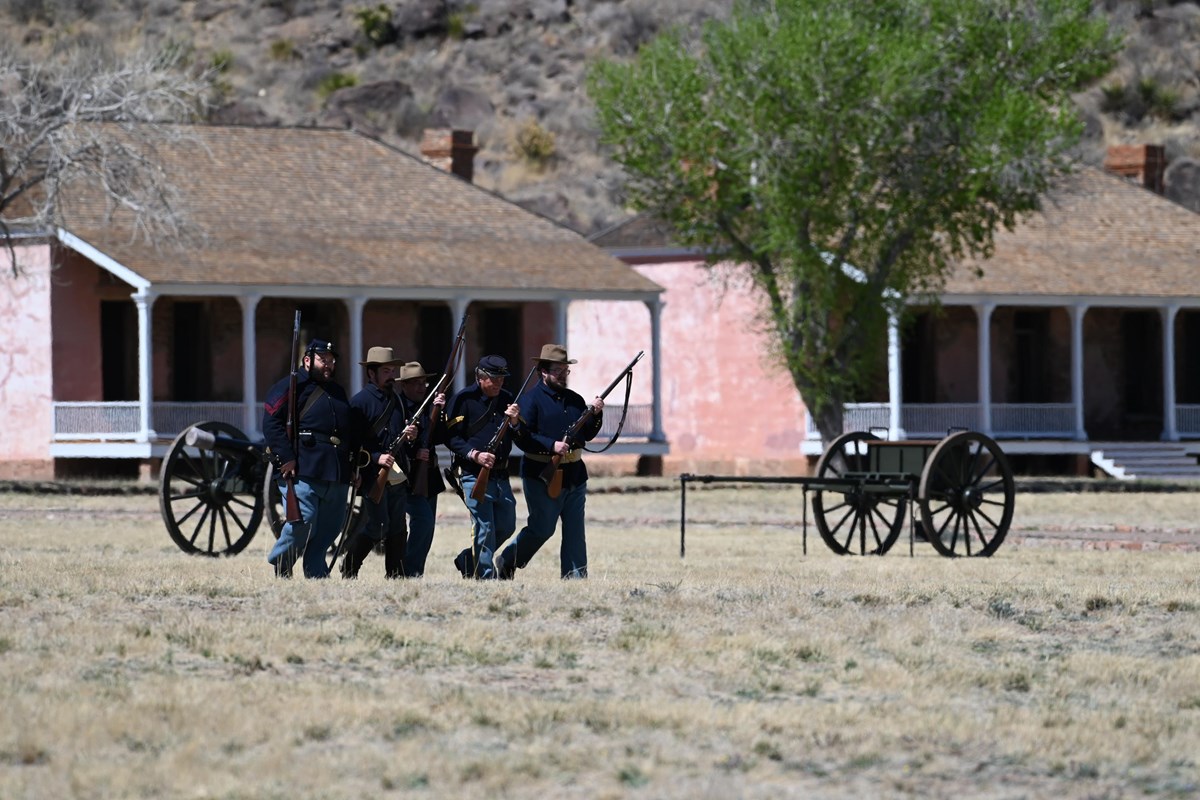A group of men in uniform holding guns marching on a parade ground.