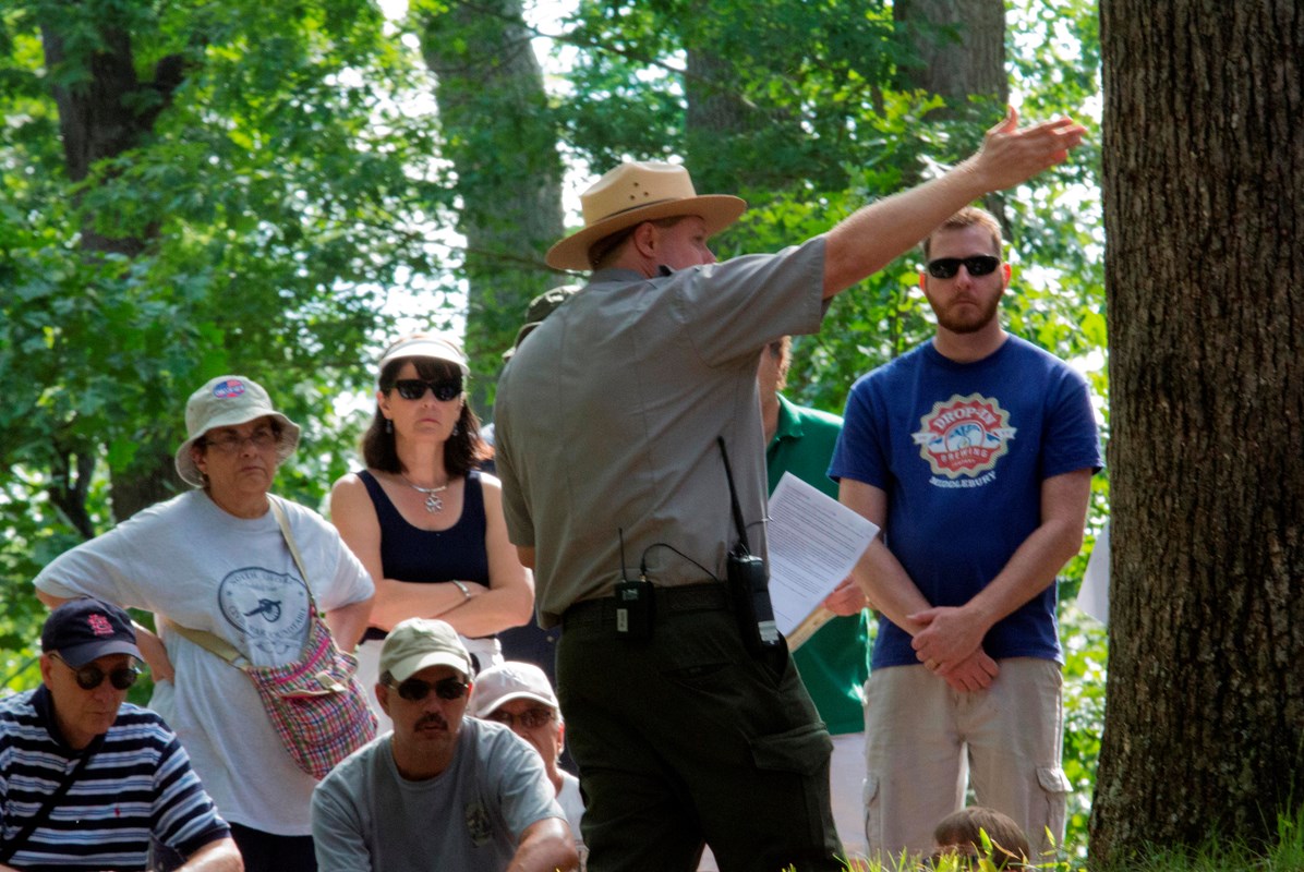 A uniformed park ranger gestures in front of a tour group.