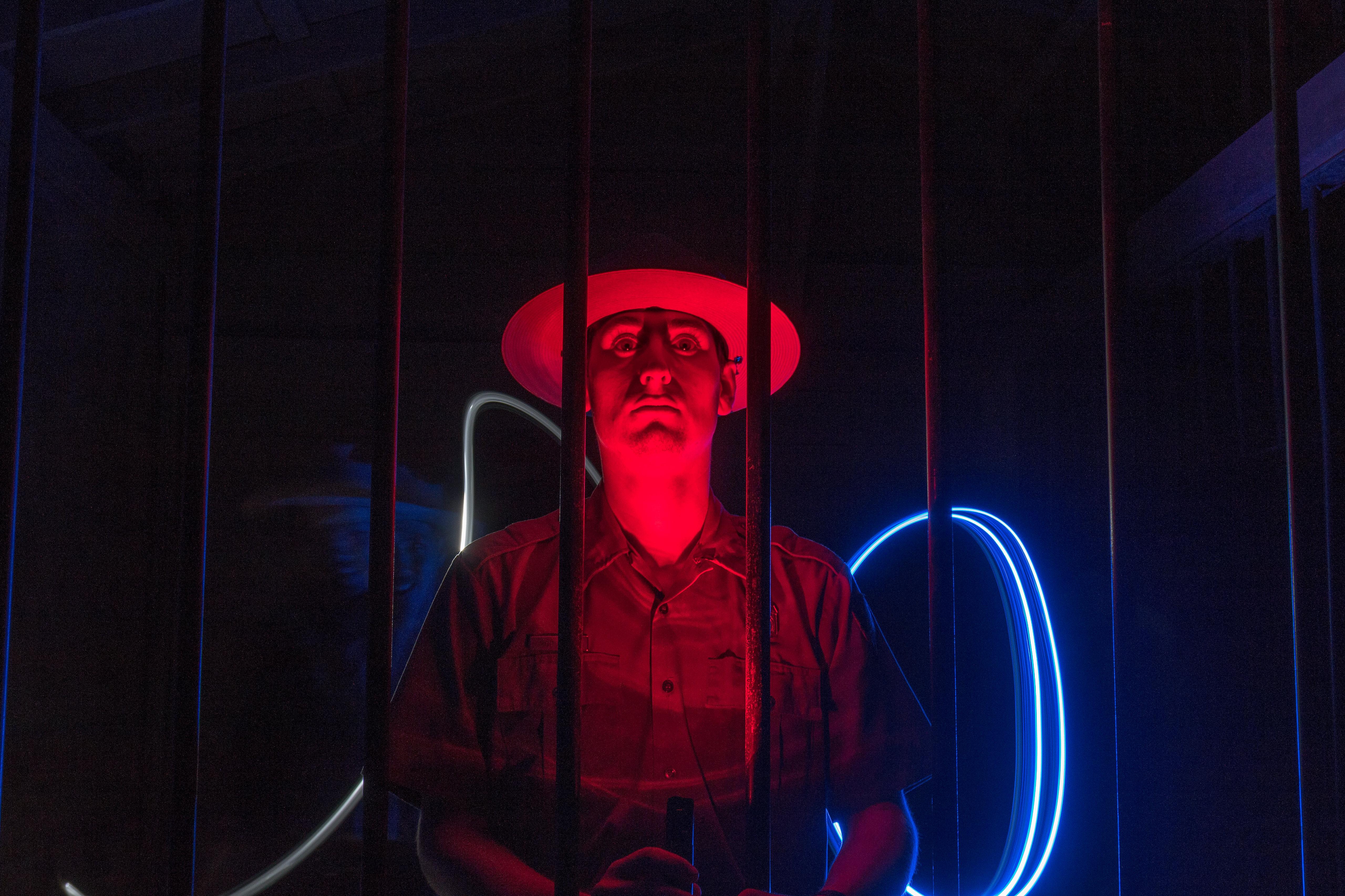 Ranger stands behind bars, there is red light shining on his face and blue light behind.