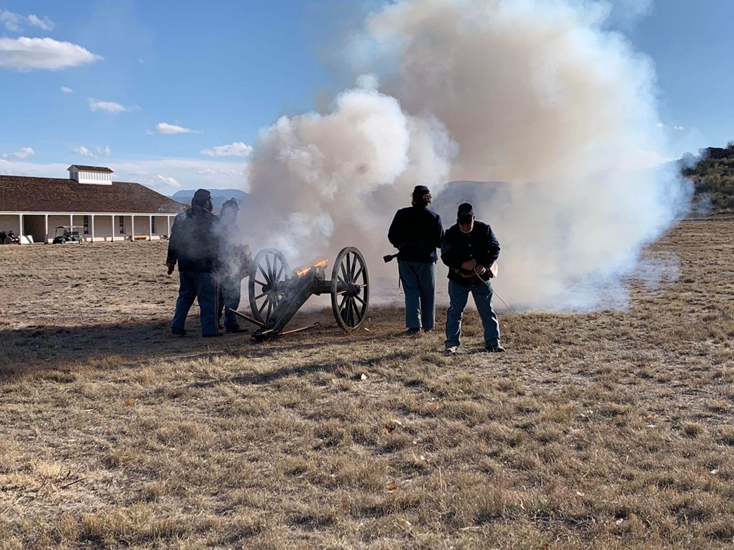 A group of men standing in a field with a cannon firing.