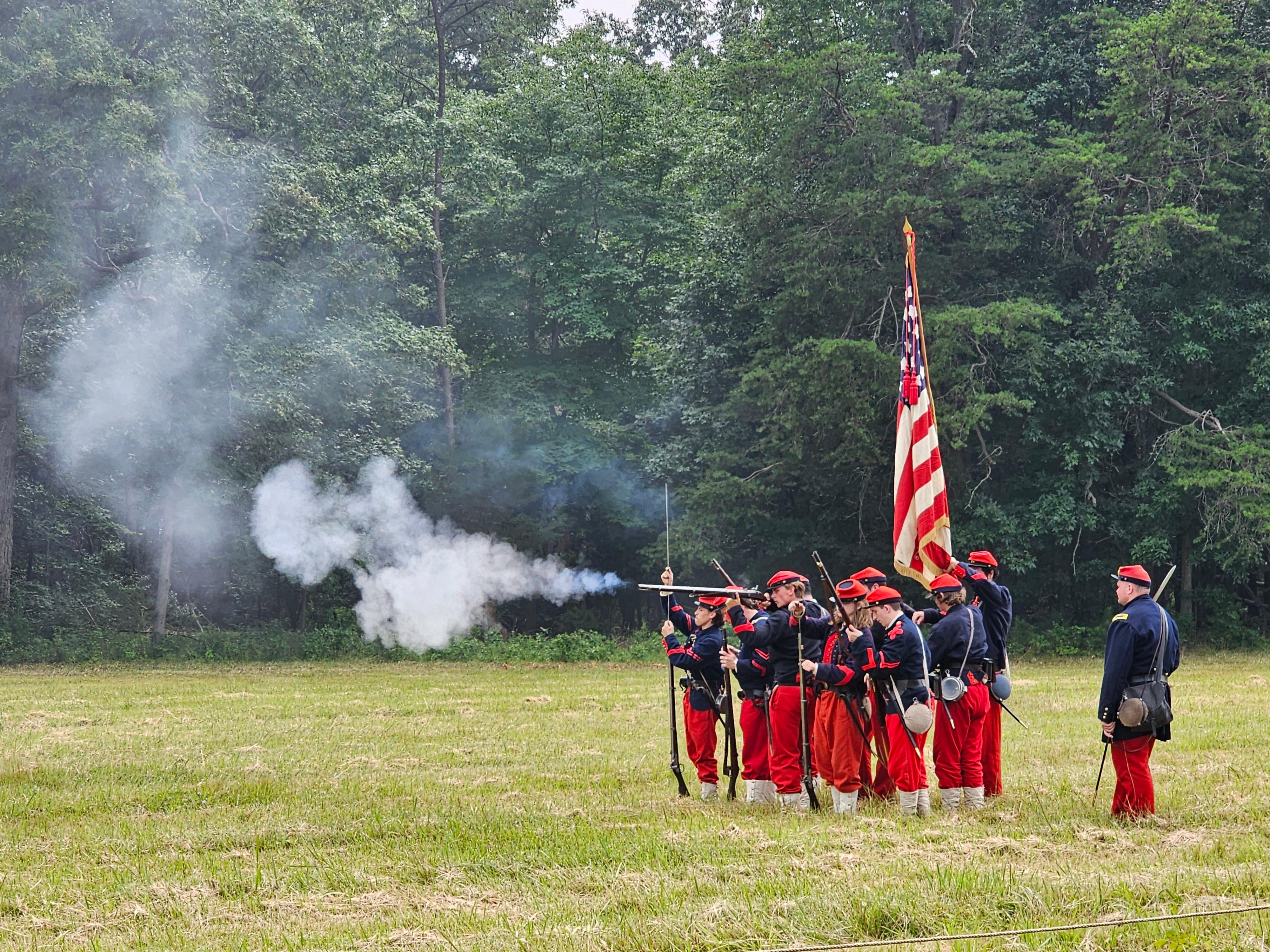 Men in the 14th Brooklyn demonstrate tactics in an open field wearing blue, red, and white.